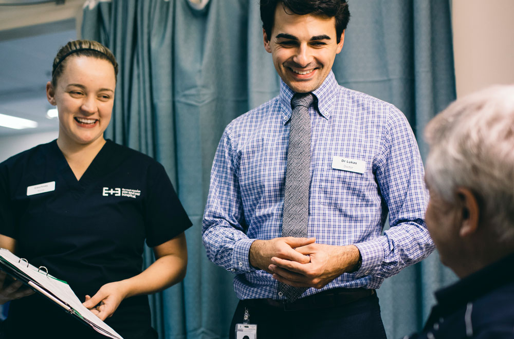 A doctor and nurse talking to a patient laying in a hospital bed
