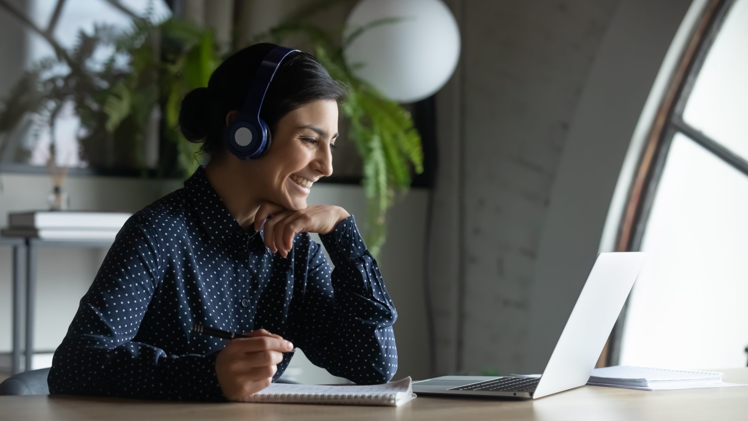Smiling woman with headphones on speaking to someone on a laptop