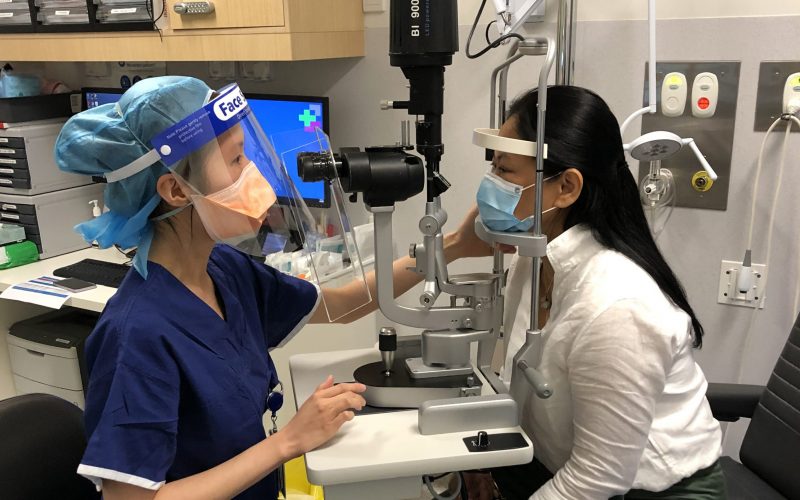 Clinician in face shield mask examining a patients eyes