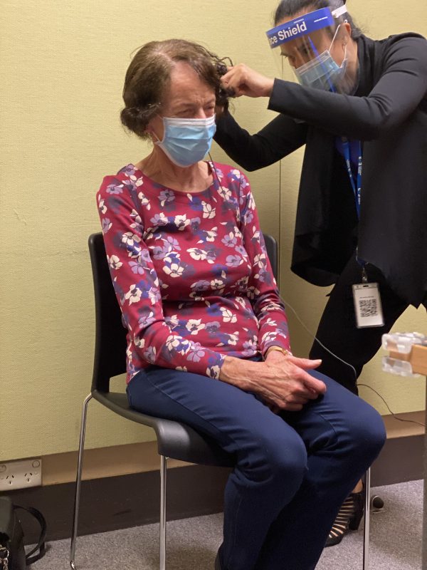 Lanna receiving her cochlear implant by a doctor at the eye and ear. she is sitting in a chair and the doctor is standing 