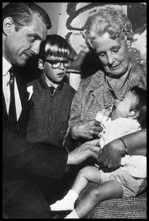 Jean LittleJohn helping an infant at the hospital, people standing watching on while she is doing it.