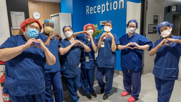 Periop nurses in scrubs and face masks smiling and making heart symbols with their hands