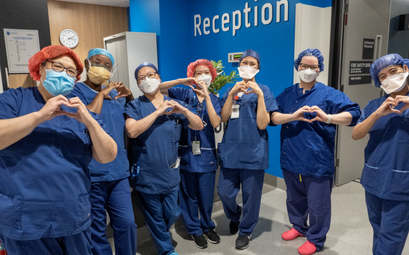 Periop nurses in scrubs and face masks smiling and making heart symbols with their hands