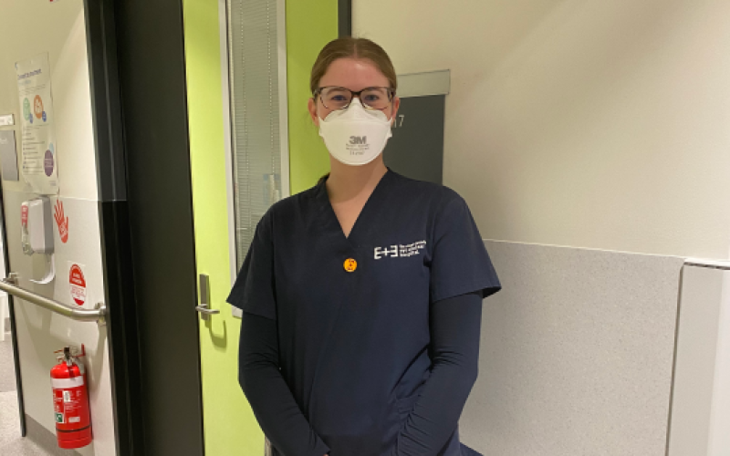 Sarah standing in one of our hospital wards, smiling with an N-95 mask on