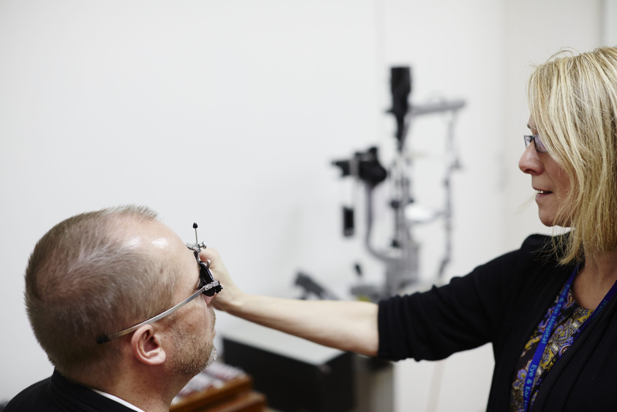 Patient having eye examined, the room is white with an eye machine in the background