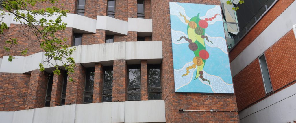 Red and white brick building with colourful painting by Wurundjeri artist Mandy Nicholson turned mural sitting up high.