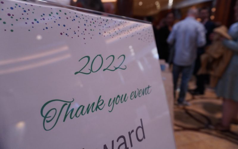 A white lamiated sign saying '2022 Thank you event' in green writing. There is a man with his back to the camera wearing a blue shirt