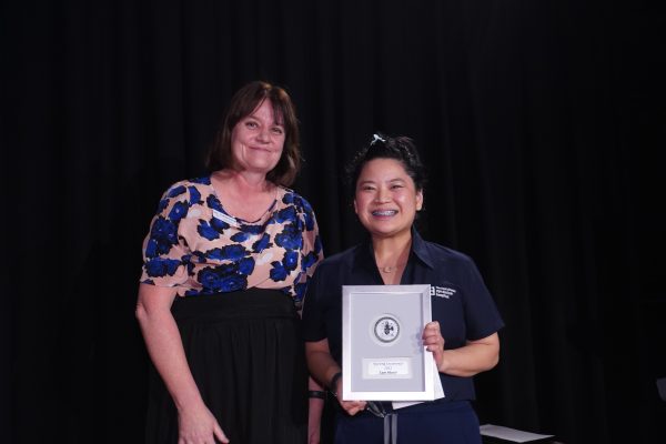 A woman in a blue and pink top standing next to a woman with black hair wearing navy scrubs holding an award