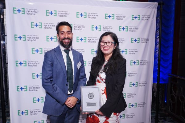 A man with black hair and a black beard wearing a navy suit standing next to a woman with long black hair in a black blazer holding an award