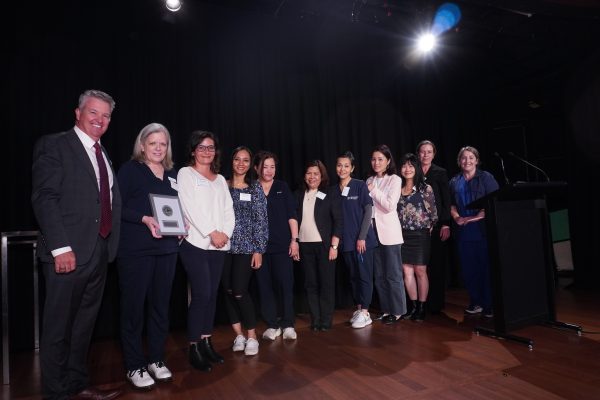 The CEO stands on the left in a black suit with grey hair, with a group of 10 women who hold an award.