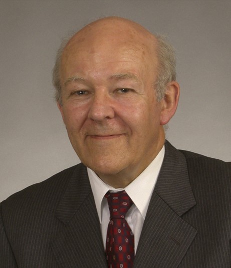 A portrait of a man in a dark grey suit jacket and red tie smiling