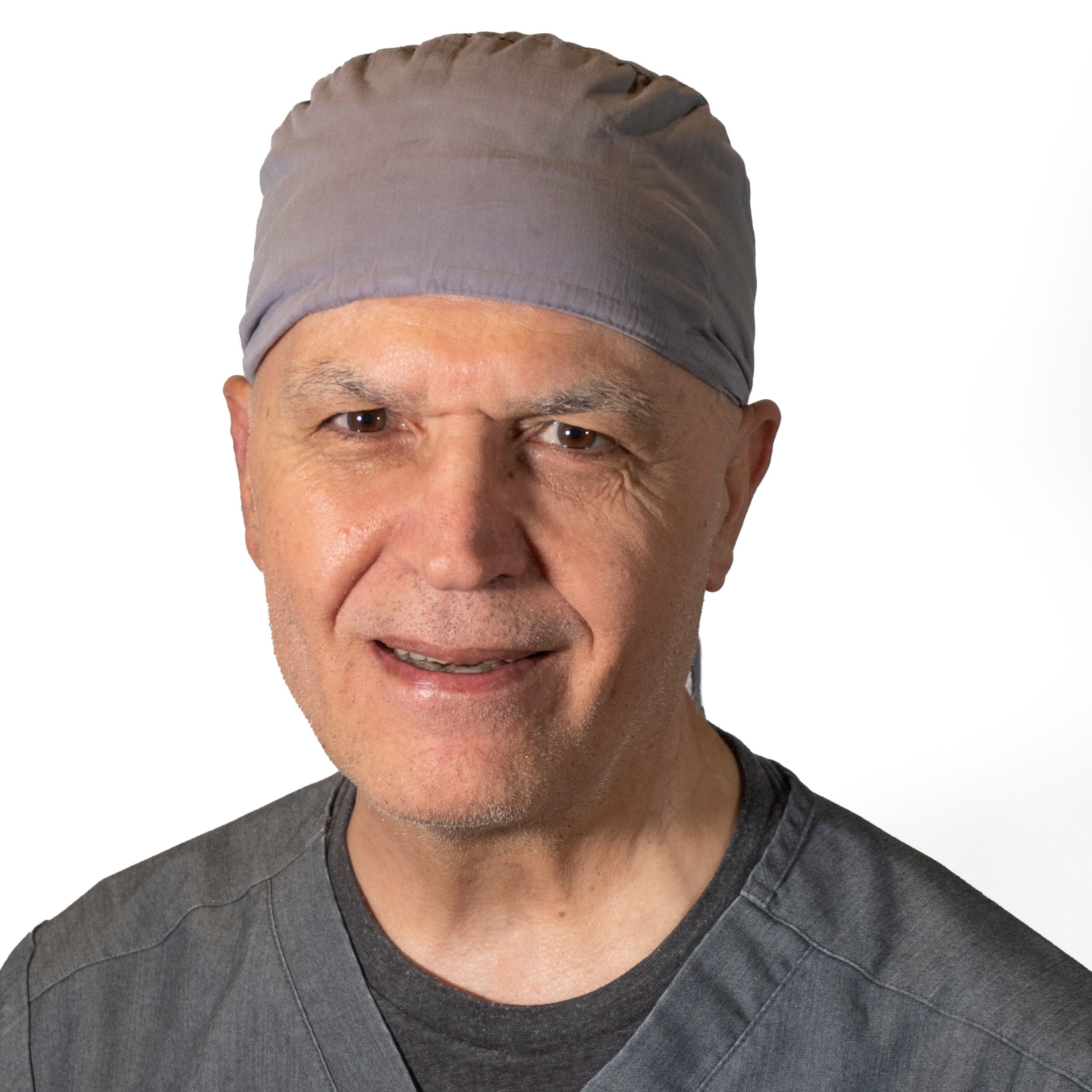 Headshot of a middle-aged male smiling wearing a doctor’s grey uniform and a doctors grey hat.