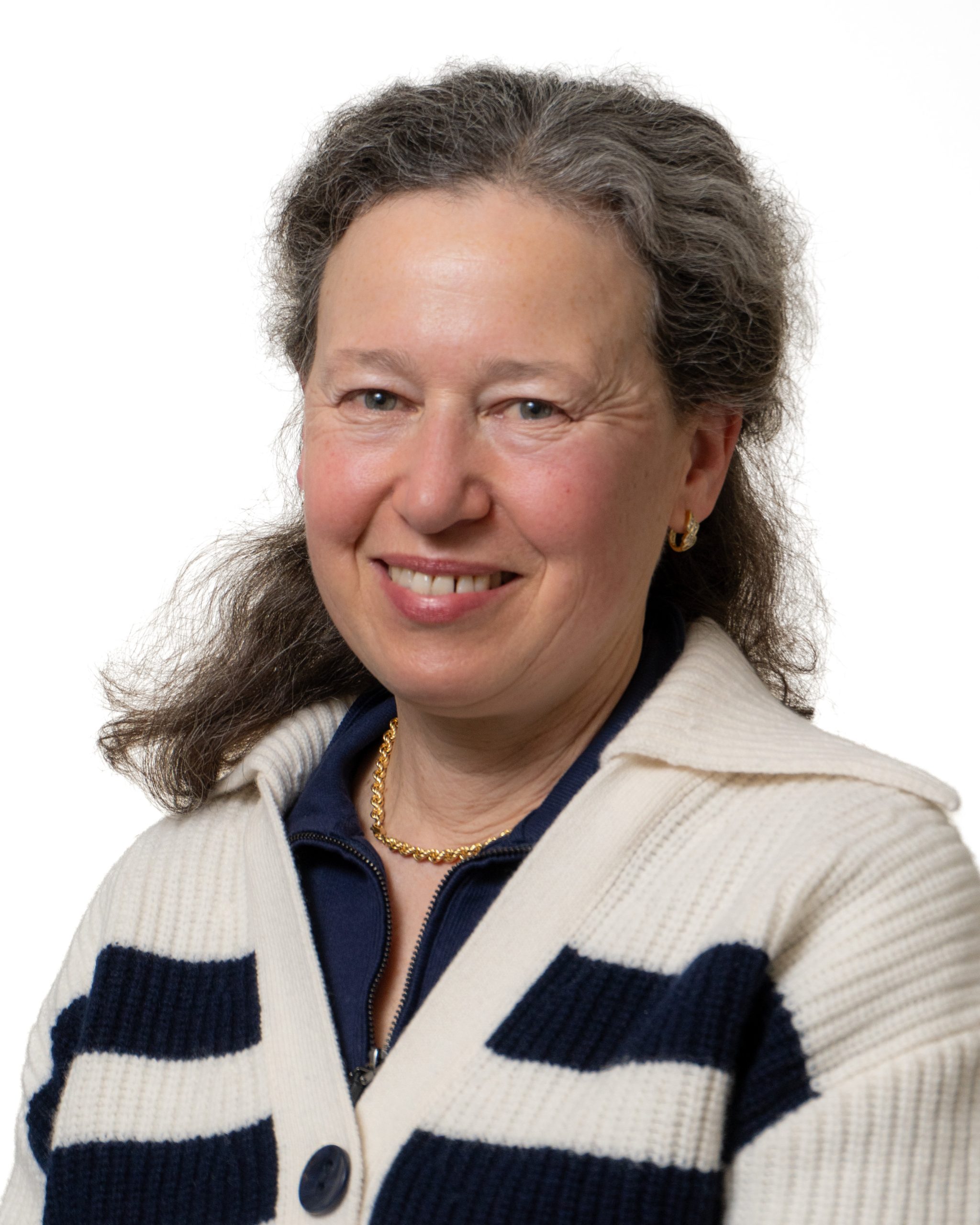 A woman with black hair is smiling while wearing a black blouse and a sweater with black and white stripes.