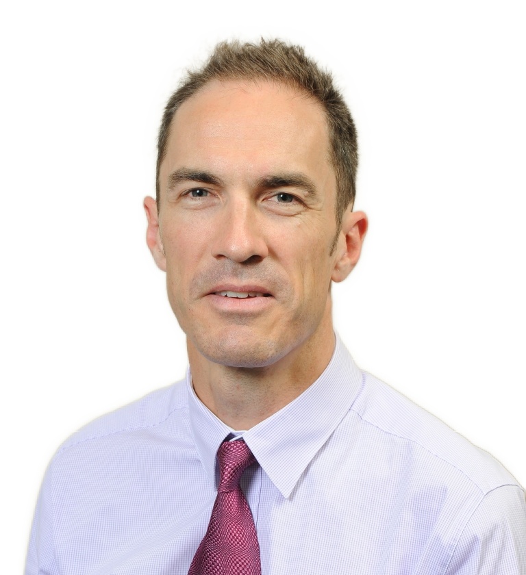 Middle man aged with brown hair, smiling. He is wearing light purple shirt with a dark purple tie.