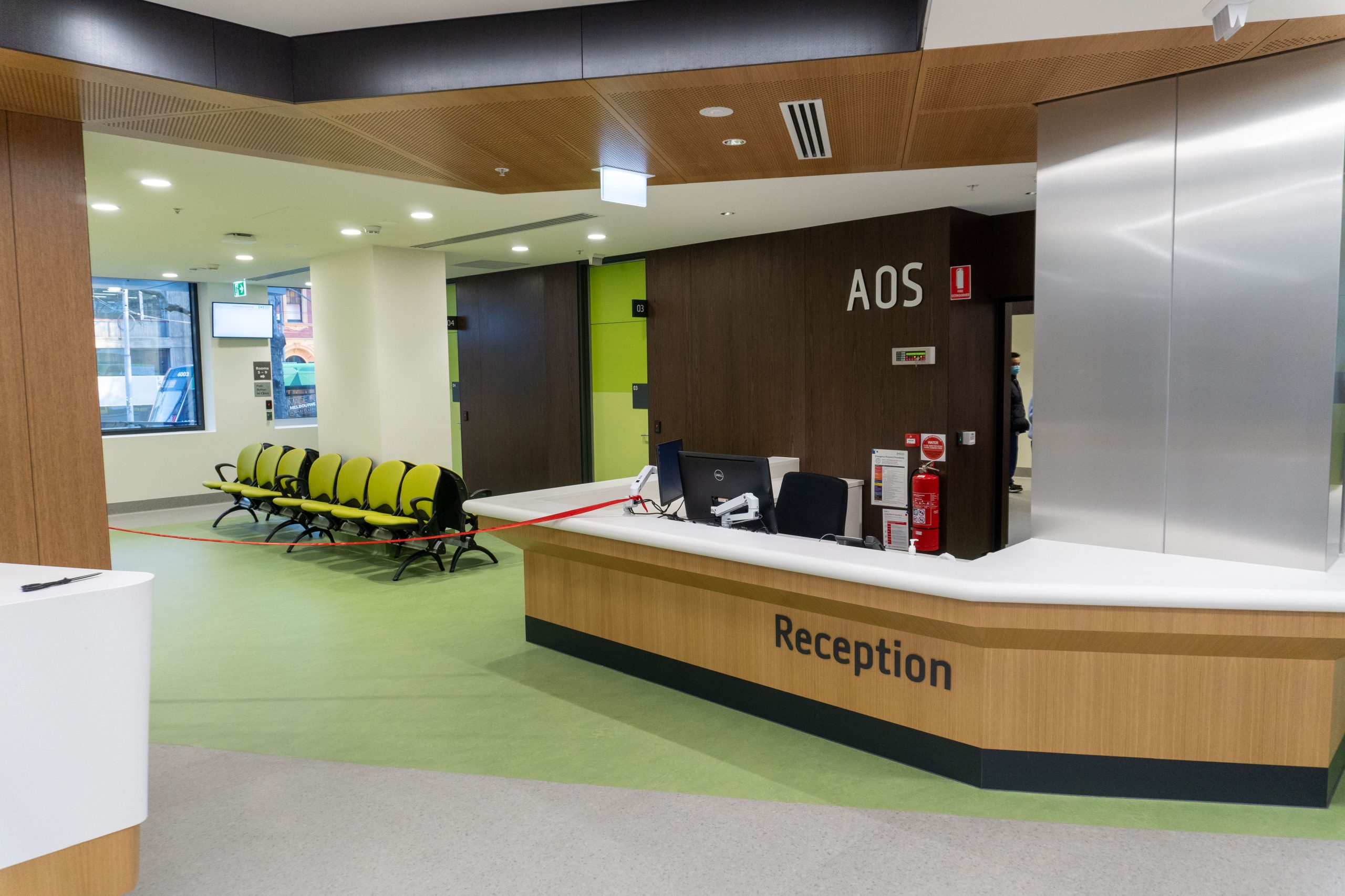 Image of a white topped reception desk with a light filled waiting room filled with green chairs