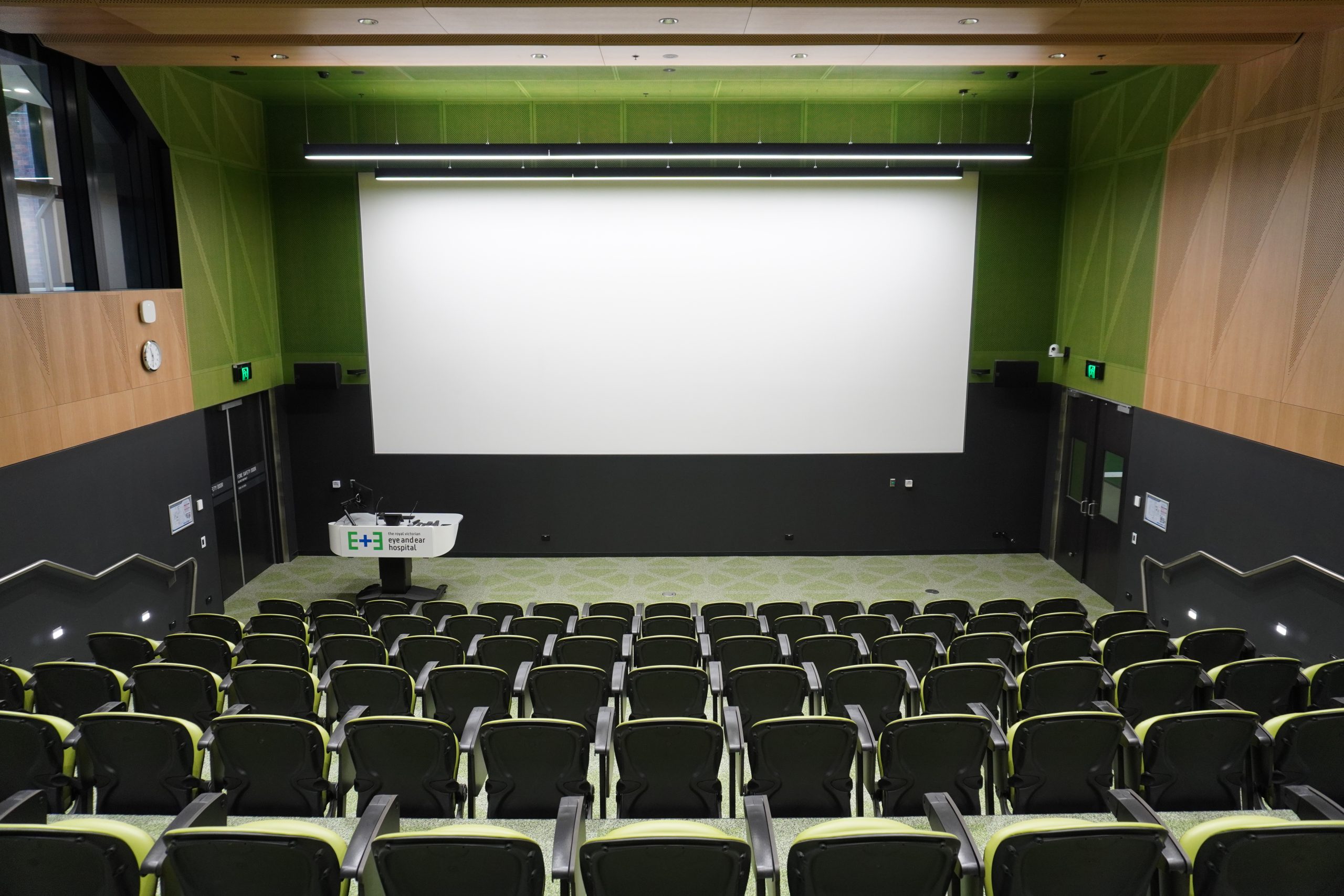 View of the Martin Family Auditorium from the back. A lectern sits down the bottom left and a large screen is front and centre