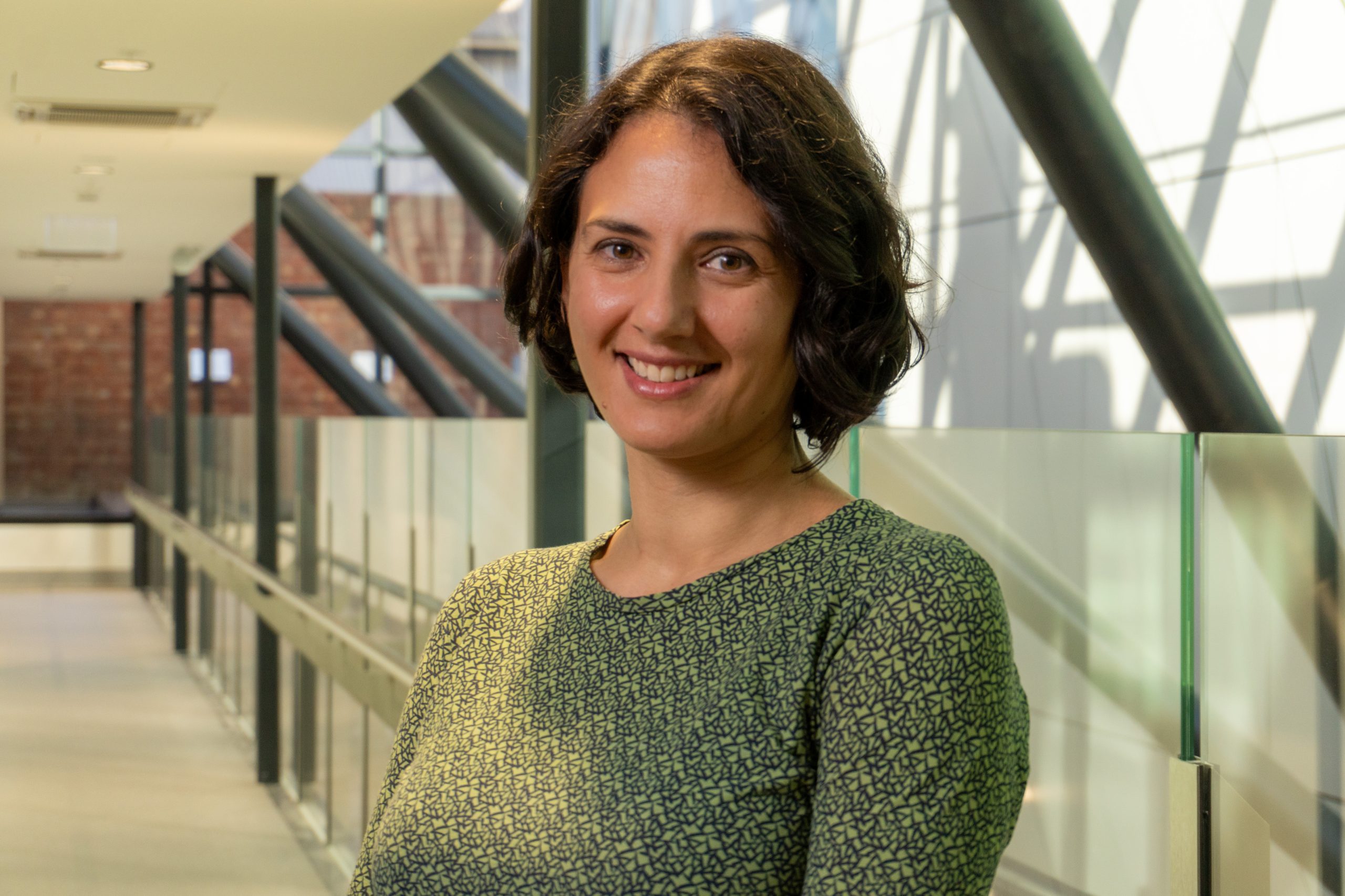 A young woman with short black hair is smiling while wearing a green blouse with black patterns.