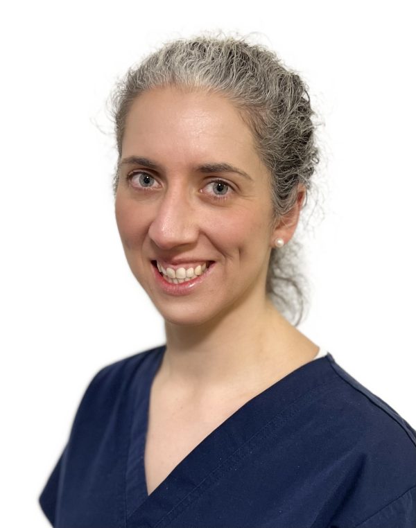 Dr Rebecca Haward wearing a navy scrub top with her hair tied back, she is smiling at the camera