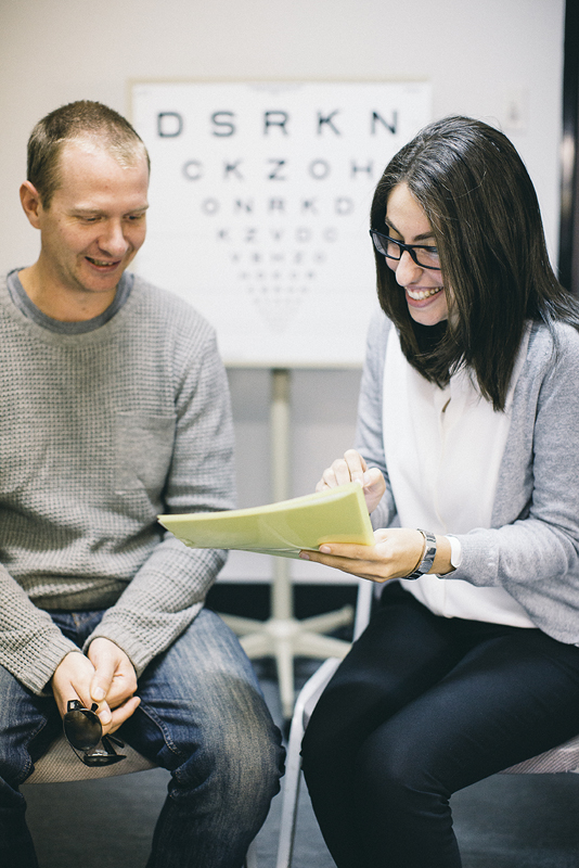 Woman sitting with a man looking at a file, an eye chart sits on the wall in the background