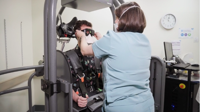 A man sitting in the Epley Omniax machine whilst a nurse adjusts the goggles on his face