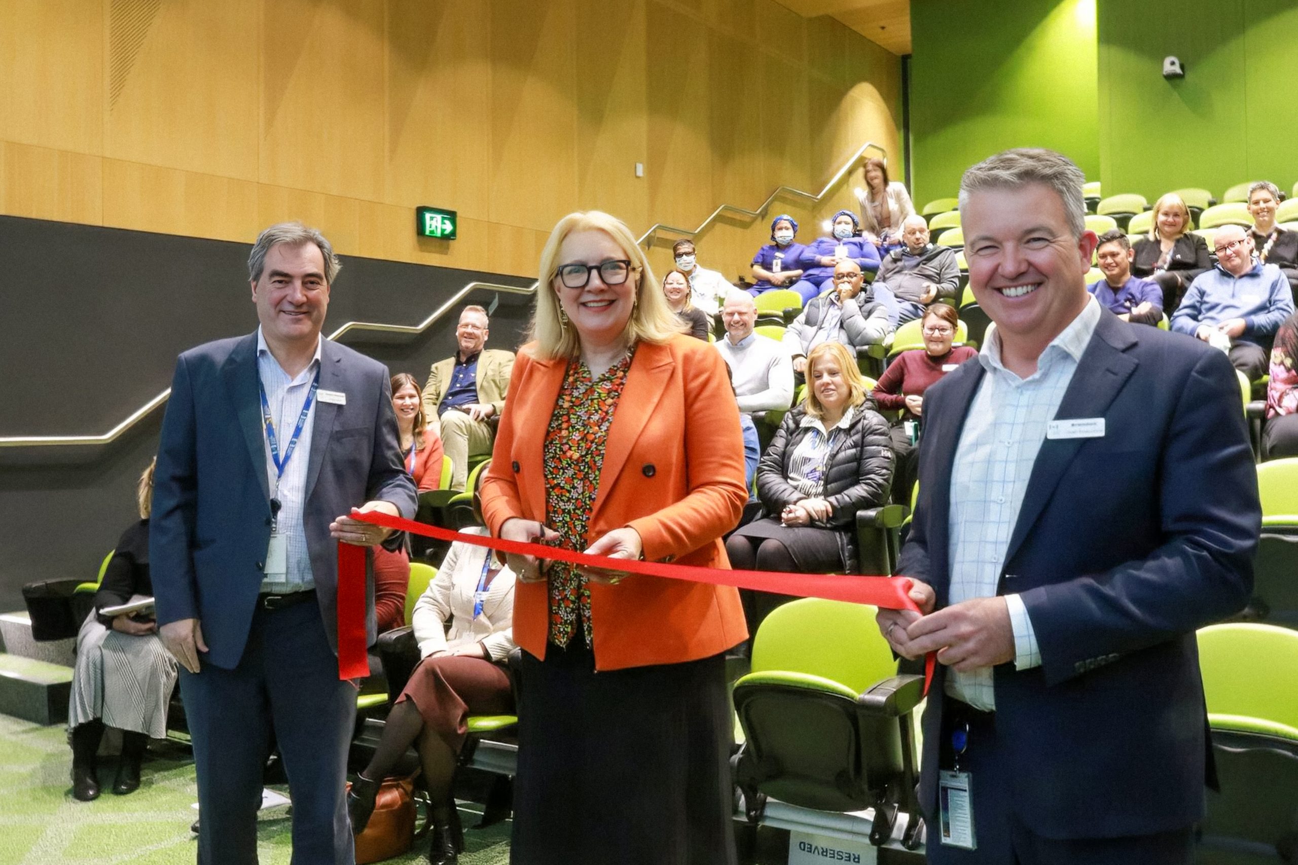 Dr Catherine Brown OAM cuts the ribbon to officially open the Martin Family Auditorium at The Royal Victorian Eye and Ear Hospital. The ribbon is held on either side by Brendon Gardner (hospital CEO) and Danny Mennuni 