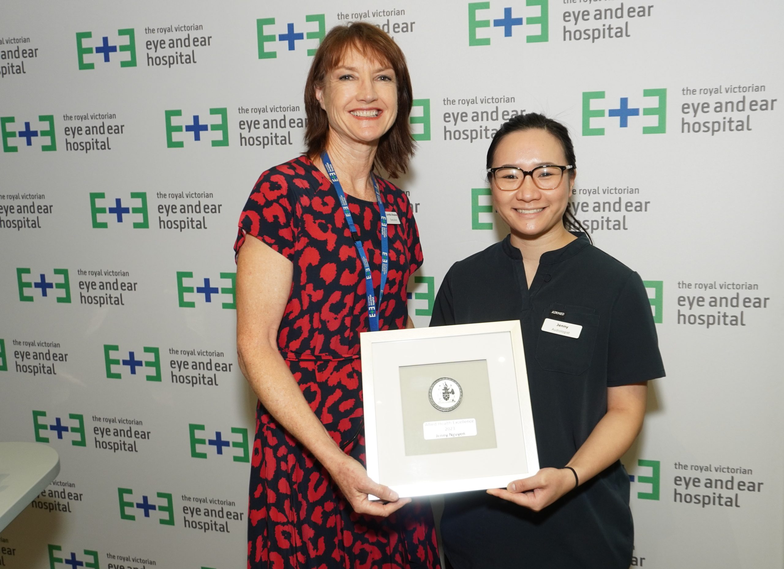 Executive Director Loretta Sheales presenting the Allied Health Award to Jenny Nguyen. They stand together, smiling, against and Eye and Ear logo backdrop