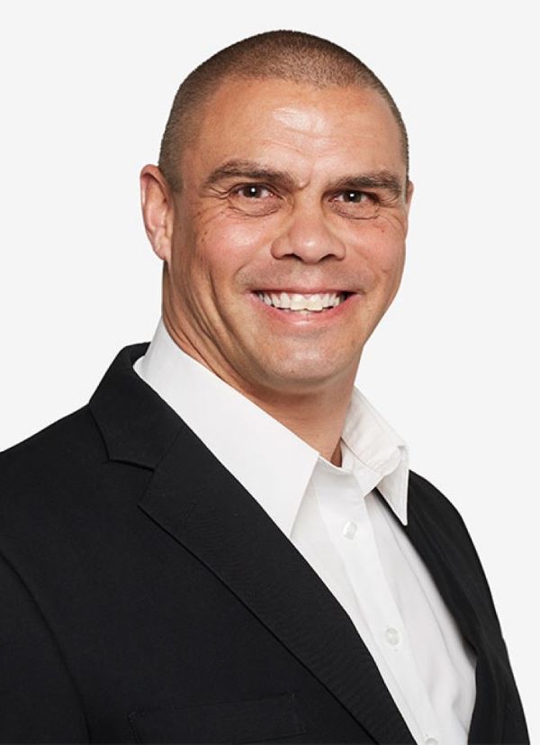 Kyle wearing a black suit with a white shirt, smiling at the camera