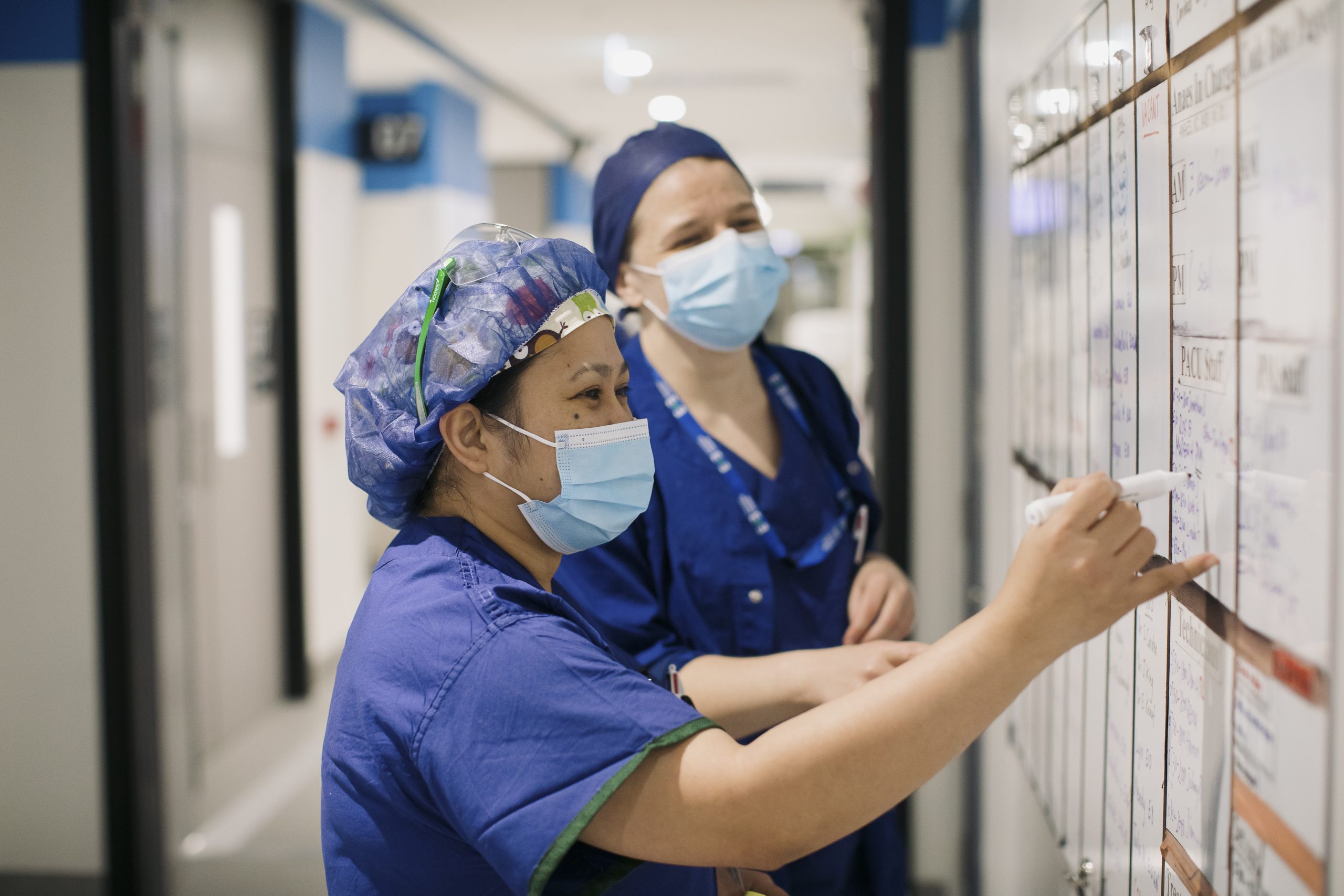 Two theater nurses wearing scrubs and masks writing on a whiteboard