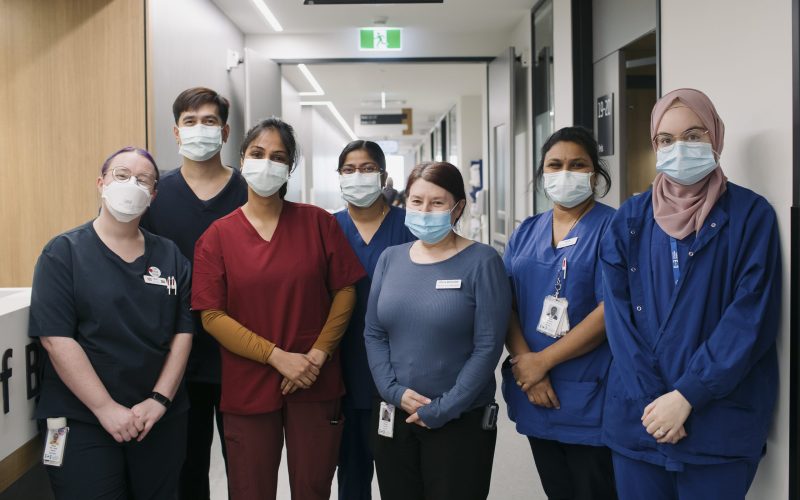 7 Inpatient ward staff standing together in the corridor, smiling with masks on.