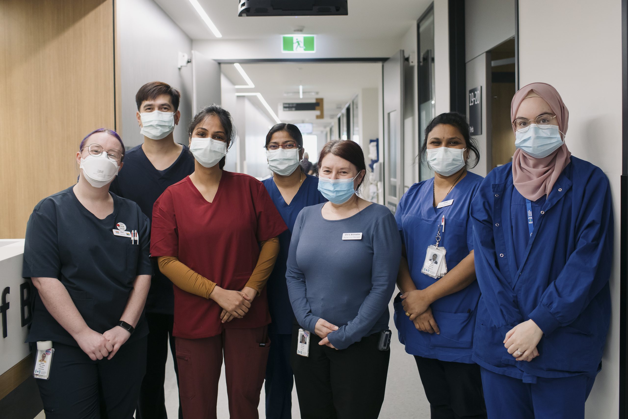 7 Inpatient ward staff standing together in the corridor, smiling with masks on.