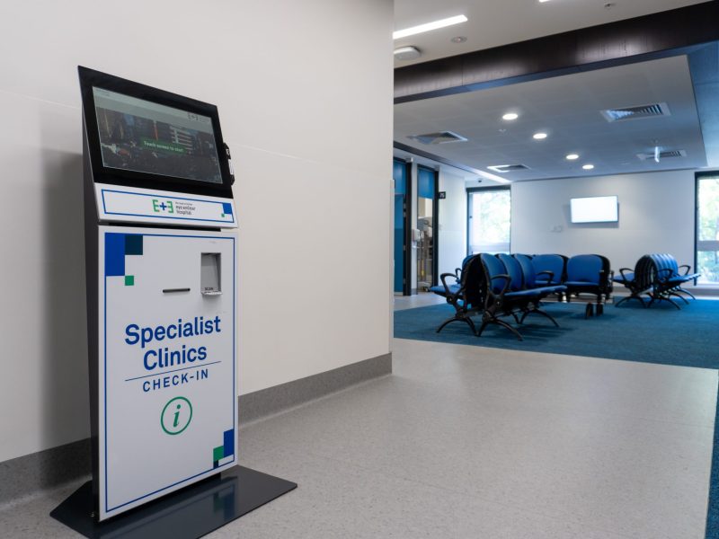Image of one of our patient self check in kiosks In the Level 1 Specialist Clinics. Patient waiting area sits in the background next to large bright windows.