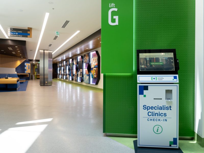 A picture of one of our patient self check-in kiosks located on the ground floor of the hospital. The EYe and Ear history wall and seating area sit in the background.