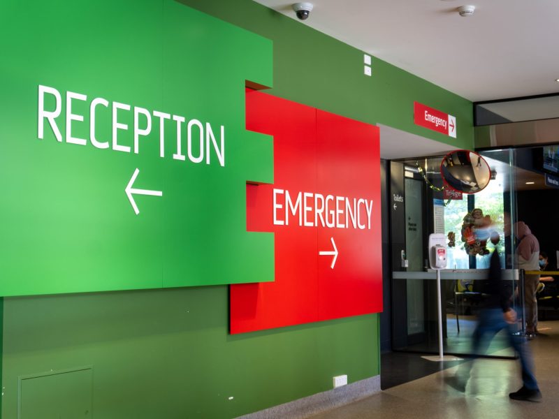 Image of the signage as you walk in from our Morrison Place entrance. A large green sign with white writing and an arrow pointing left reads 'Reception' and a red panel with white writing and an arrow pointing right says 'Emergency'.