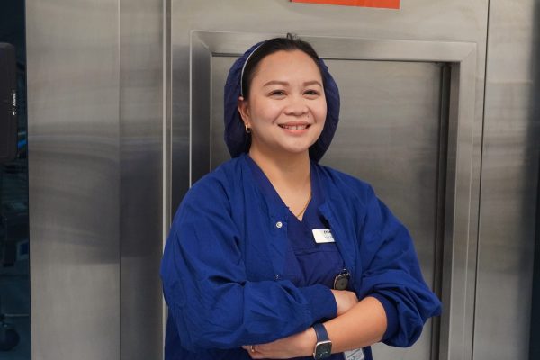 Nurse Ethel standing against a silver machine in her blue scrubs and hairnet.
