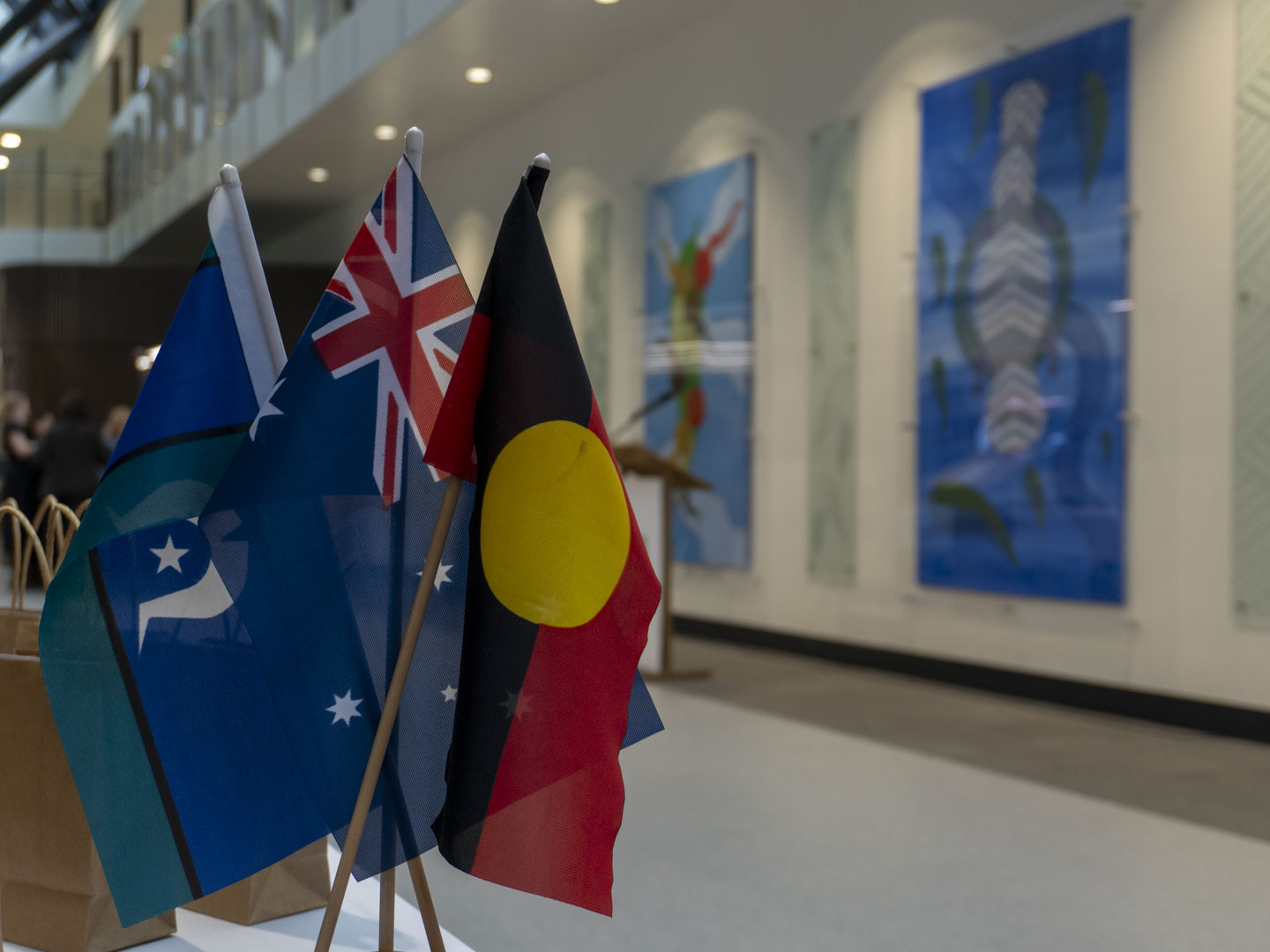The Aboriginal, Torres Strait Islander and Australian flags hang in front of two large pieces of Aboriginal artwork.