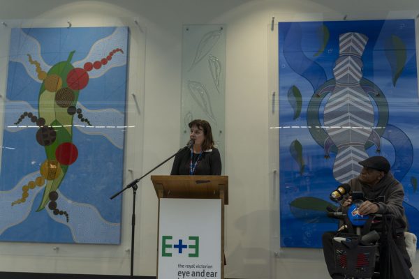 Leanne Turner, Executive Director Operations and Chief Nursing Officer, speaks at a podium between two large pieces of Aboriginal artwork