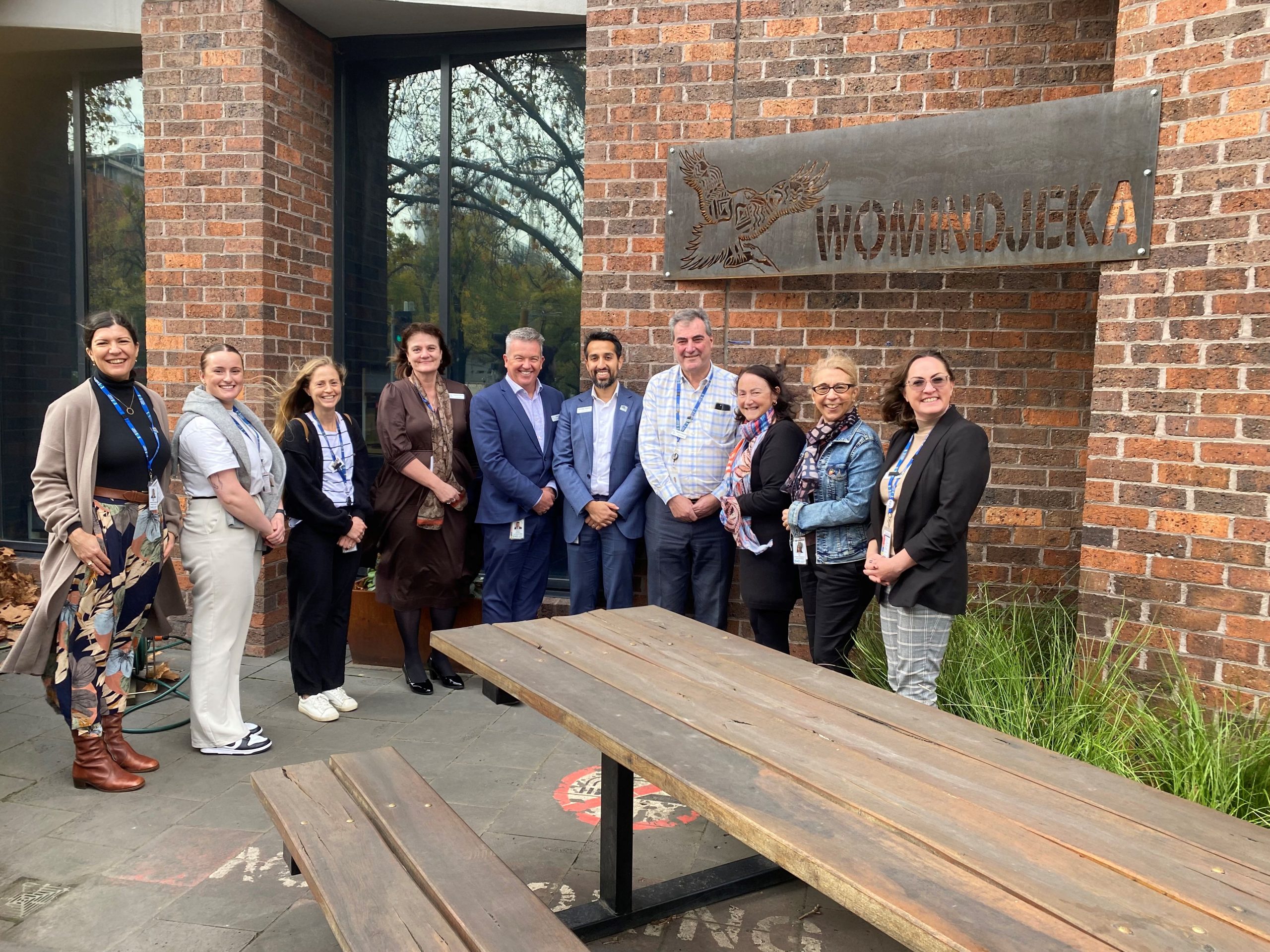 Our Mirring Ba Wirring team standing with a group of Executive and staff members on an Aboriginal Art tour of the hospital during Reconciliation Week. They're standing in our Welcome Space side by side beneath our newest Womindjeka sign on the wall featuring a Bunjil (eagle).