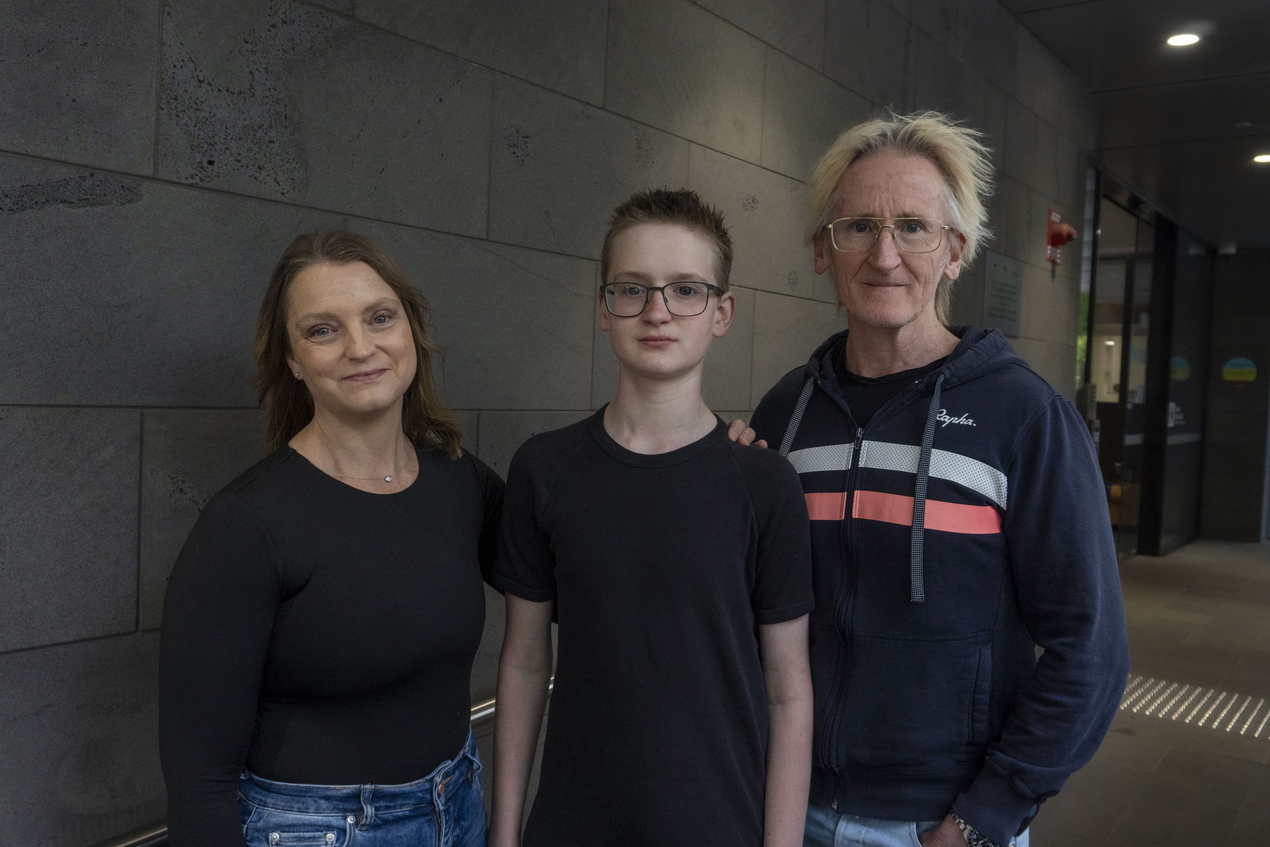 A young man stands between his parents, smiling at the camera