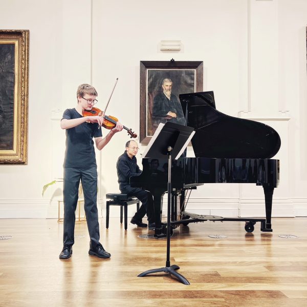 A young man plays the violin, accompanied by a pianist