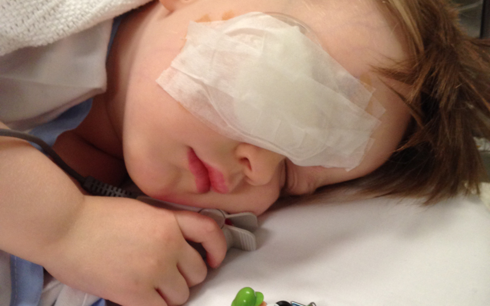 A young boy lies in a hospital bed with an eye patch