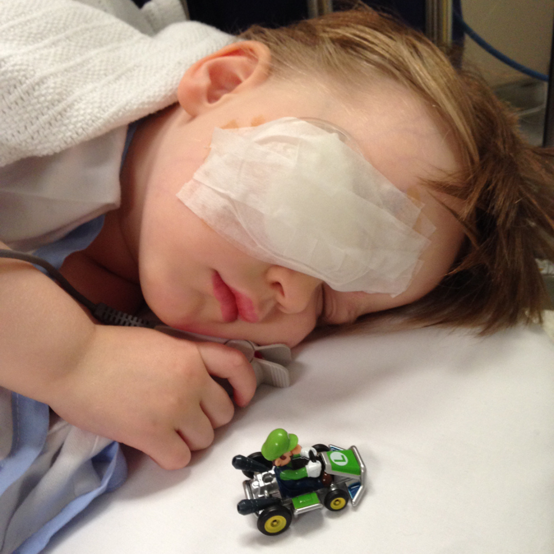 A young boy lies in a hospital bed with an eye patch