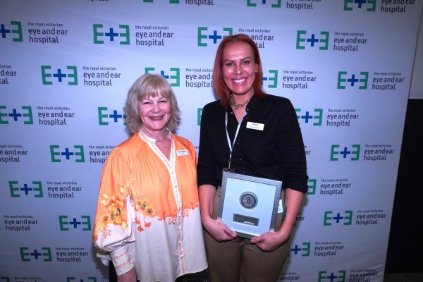 A blonde woman in a yellow and white shirt stands next to a tall women with red hair holding an award