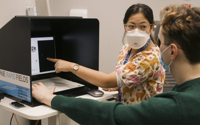 A woman points to a screen while speaking with a man wearing an eye patch.