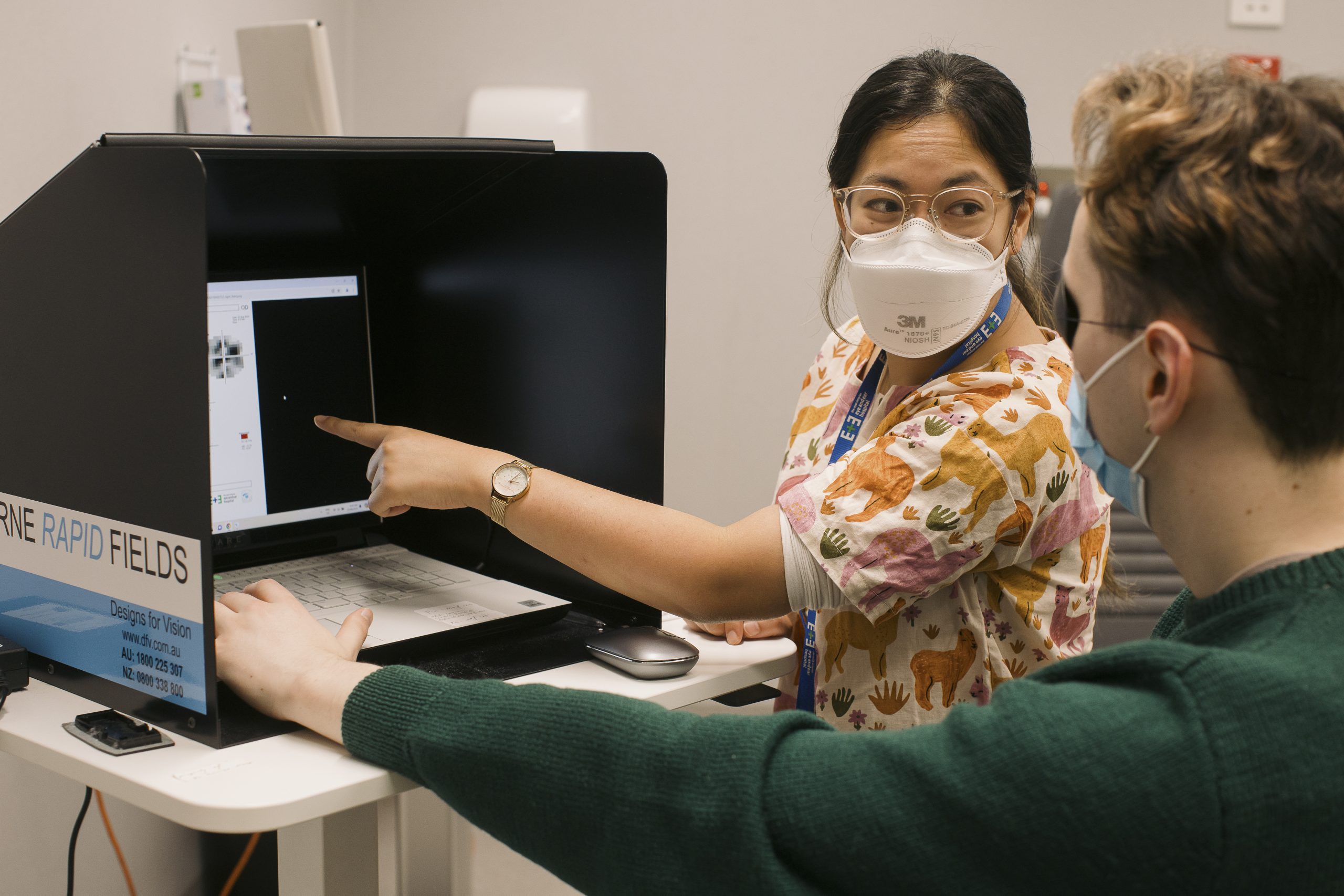 A woman points to a screen while speaking with a man wearing an eye patch.