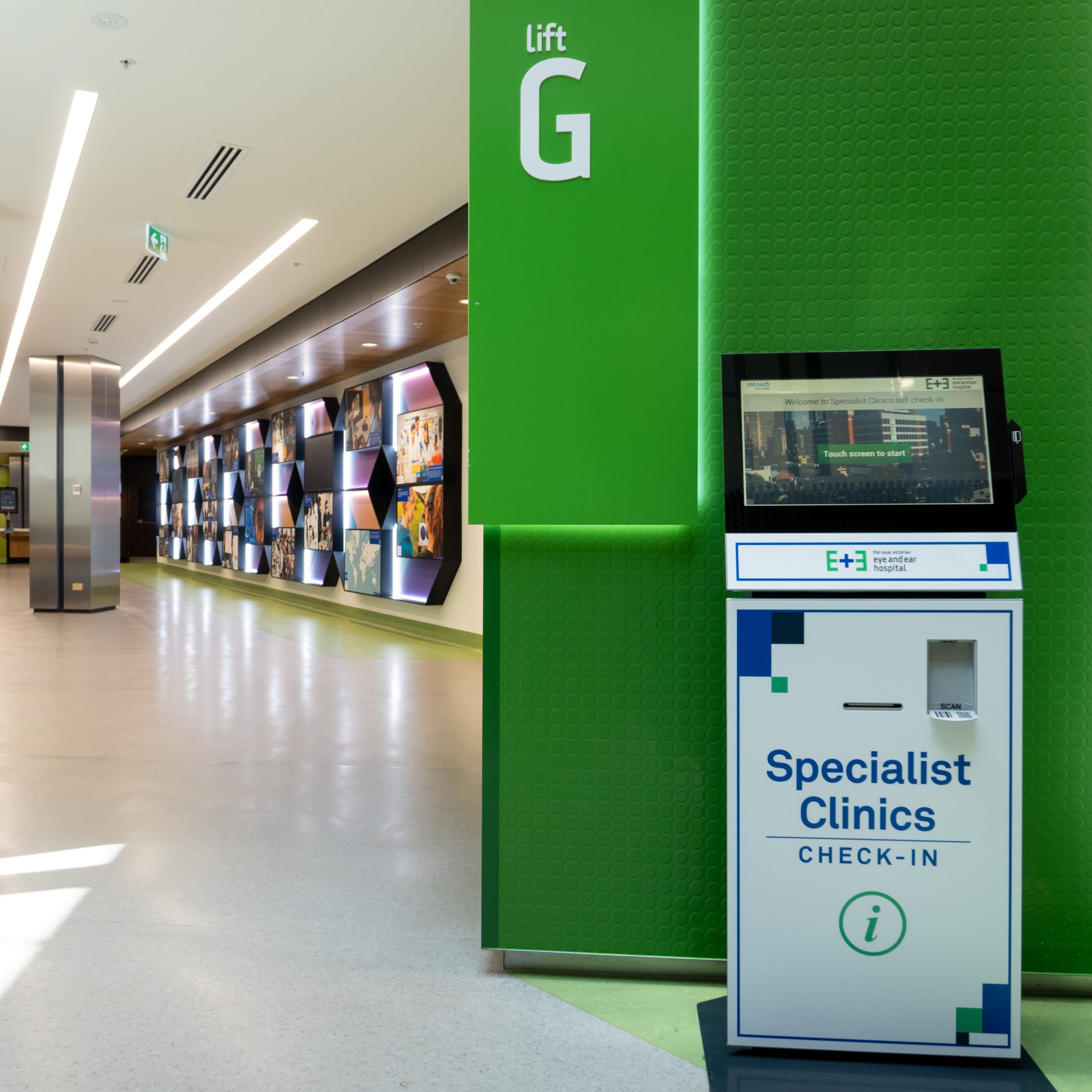 A picture of one of our patient self check-in kiosks located on the ground floor of the hospital. The EYe and Ear history wall and seating area sit in the background.