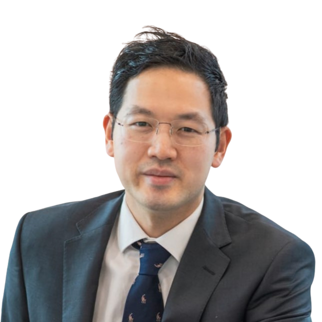 A man with dark hair, dark suit and glasses smiles at the camera