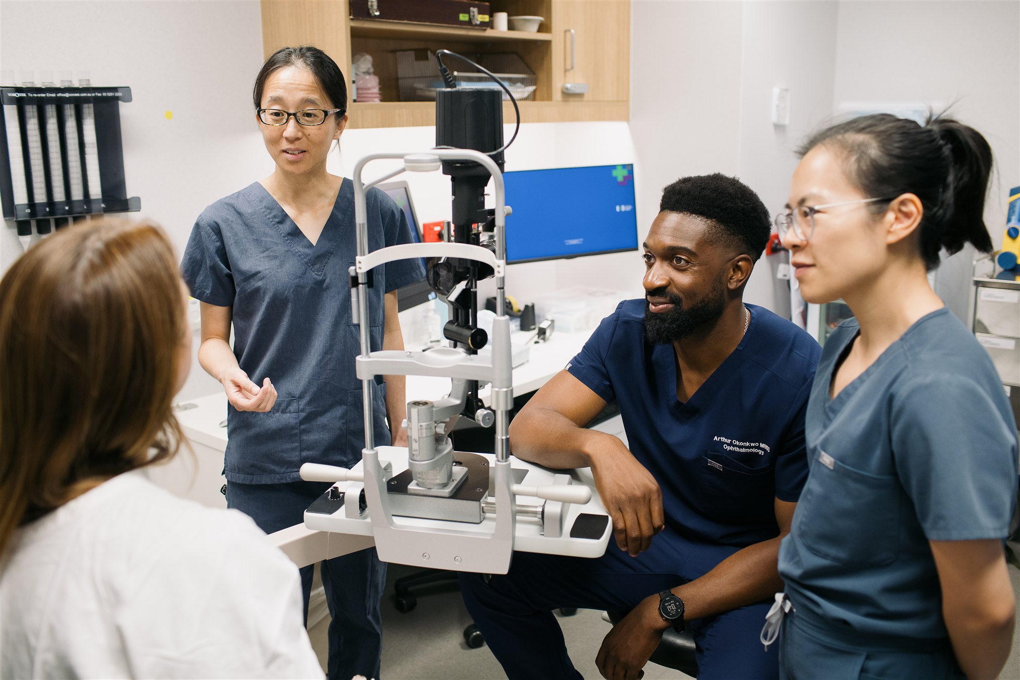 Three eye doctors in training discussions with a patient at a slit lamp.