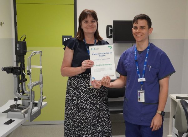 A man in blue scrubs holding a certificate with a woman in a black top and patterned skirt