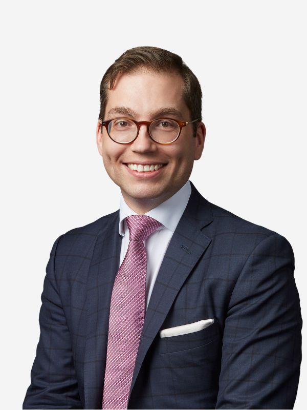 Headshot of a man in glasses smiling at the camera wearing a navy jacket, white shirt and pink tie.