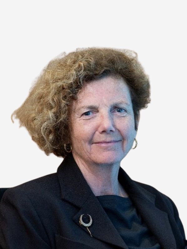 A woman with light brown curly hair smiles at the camera against a white background wearing a black top and blazer